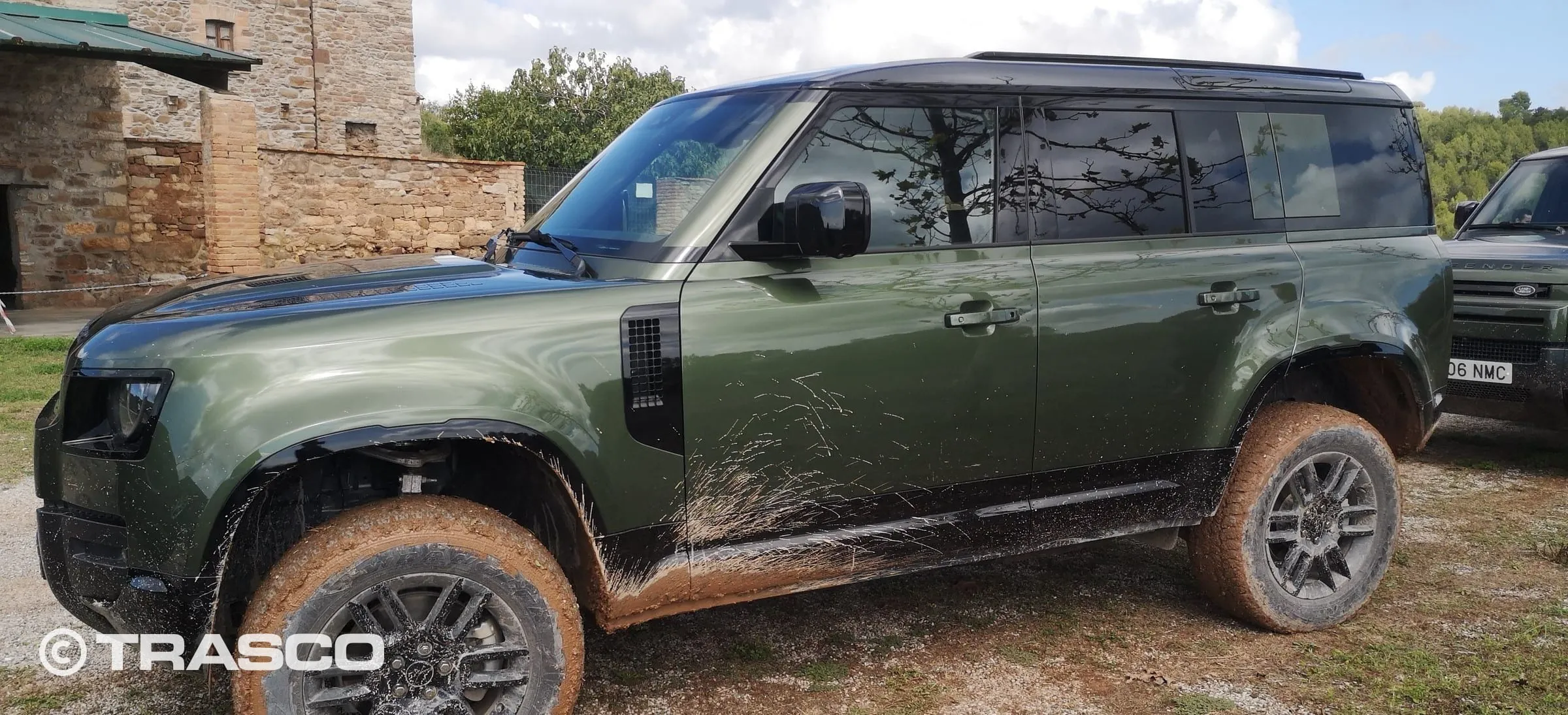 Defender mit Schlamm an Rädern und Schwellern vor einem Natursteingebäude in Les Comes