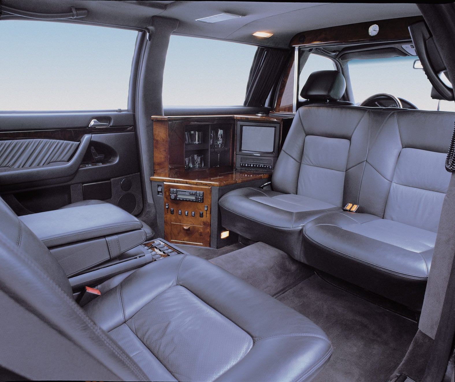 Club seating facing a partition wall with monitor and audio controls in an extended limousine