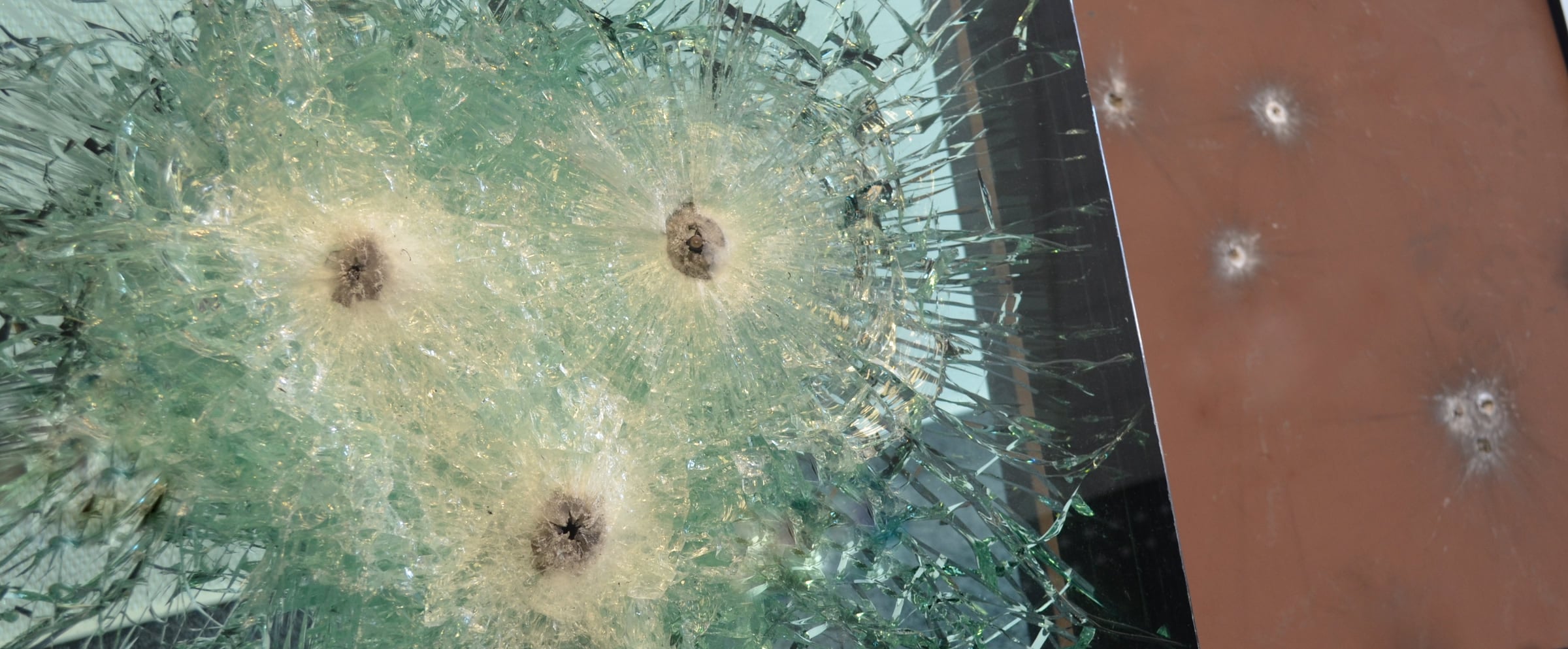 Prüfmuster aus ballistischem Glas und ballistischem Stahl mit Einschüssen nach der Prüfung